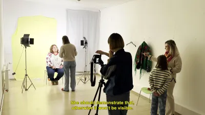 A film set showing a person talking to an actor in front of a backdrop, a person looking through a camera, and two people at the side gesturing. 