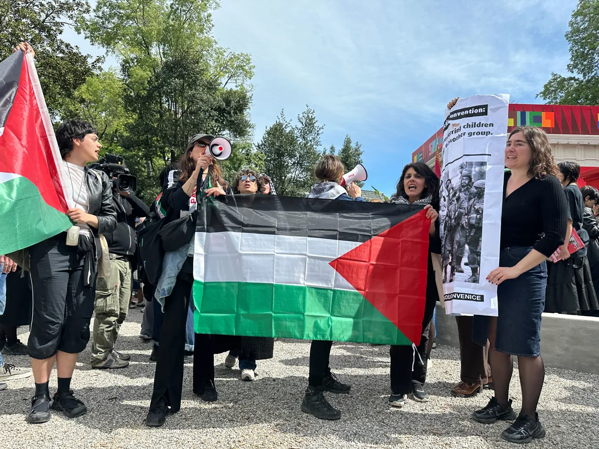 Two sets of people hold up Palestinian flags, with two people shouting into megaphones.
