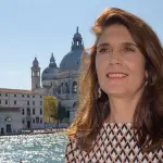 A woman smiles with a grand church and canal behind her.