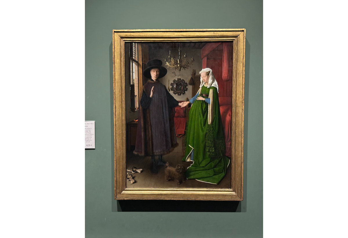 A painting of a man in a big hat holding the hand of a woman dressed in rich green robes. The painting is bordered in a gold frame.