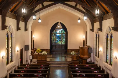View of the interior of a chapel with a stained glass window at back.