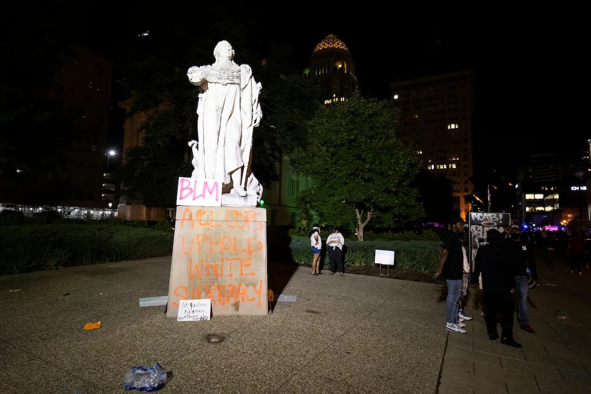 A graffitied monument in a park with a sign reading