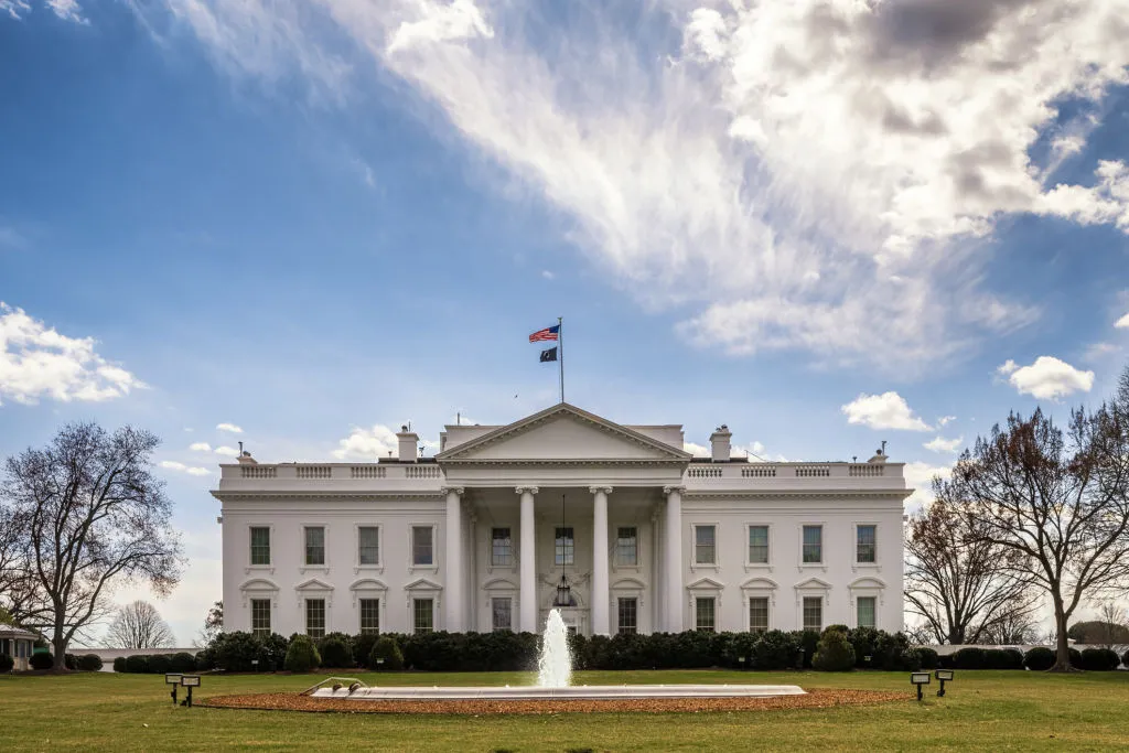 A white columned building with a fountain in front of it.