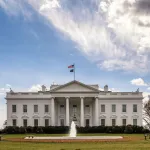 A white columned building with a fountain in front of it.