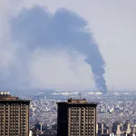 TOPSHOT - Smoke billows in the distance from an oil refinery following an Israeli strike on the Iranian capital Tehran on June 17, 2025. Israel and Iran exchanged fire again, the fifth day of strikes in their most intense confrontation in history, fuelling fears of a drawn-out conflict that could engulf the Middle East. (Photo by ATTA KENARE / AFP) (Photo by ATTA KENARE/AFP via Getty Images)