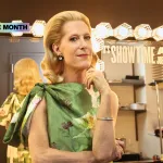 A blond woman in a green dress in front of a vanity mirror, backstage