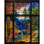 A monumental stained glass window showing a nature scene of a forrest, stream, and mountain the background.
