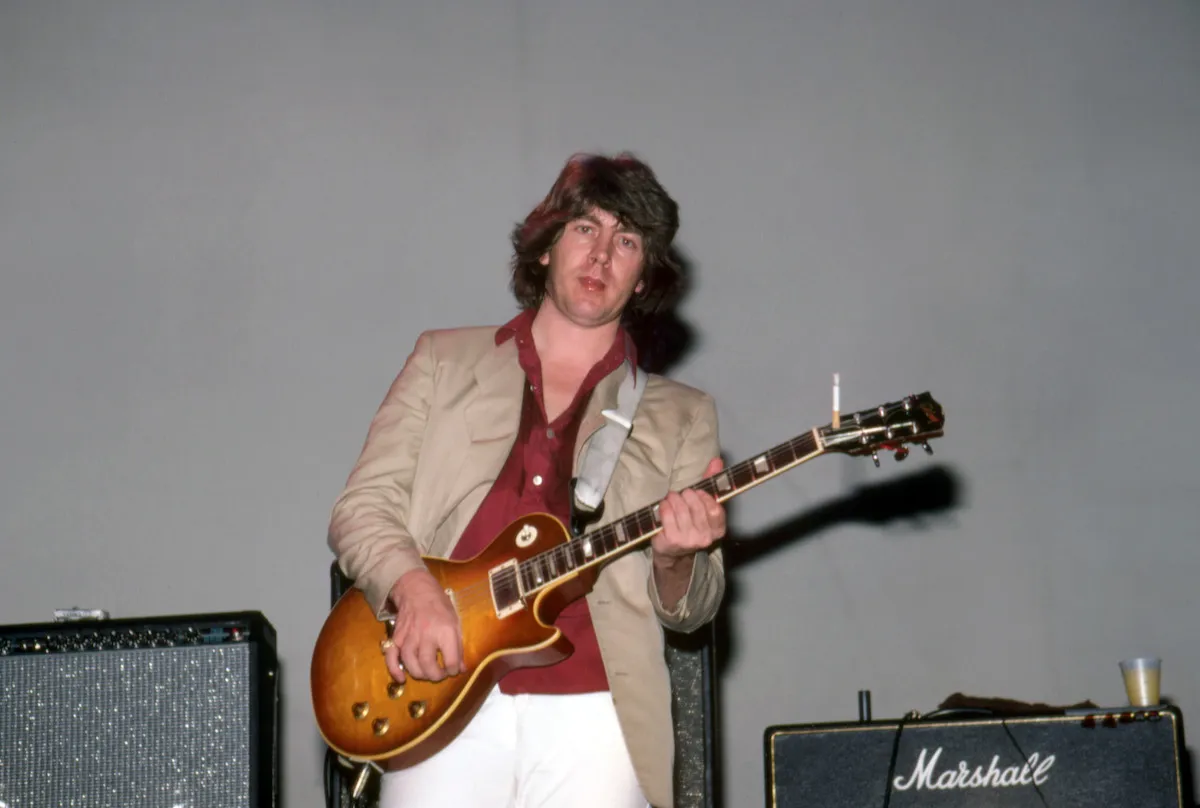 A man holding a guitar before an amp.