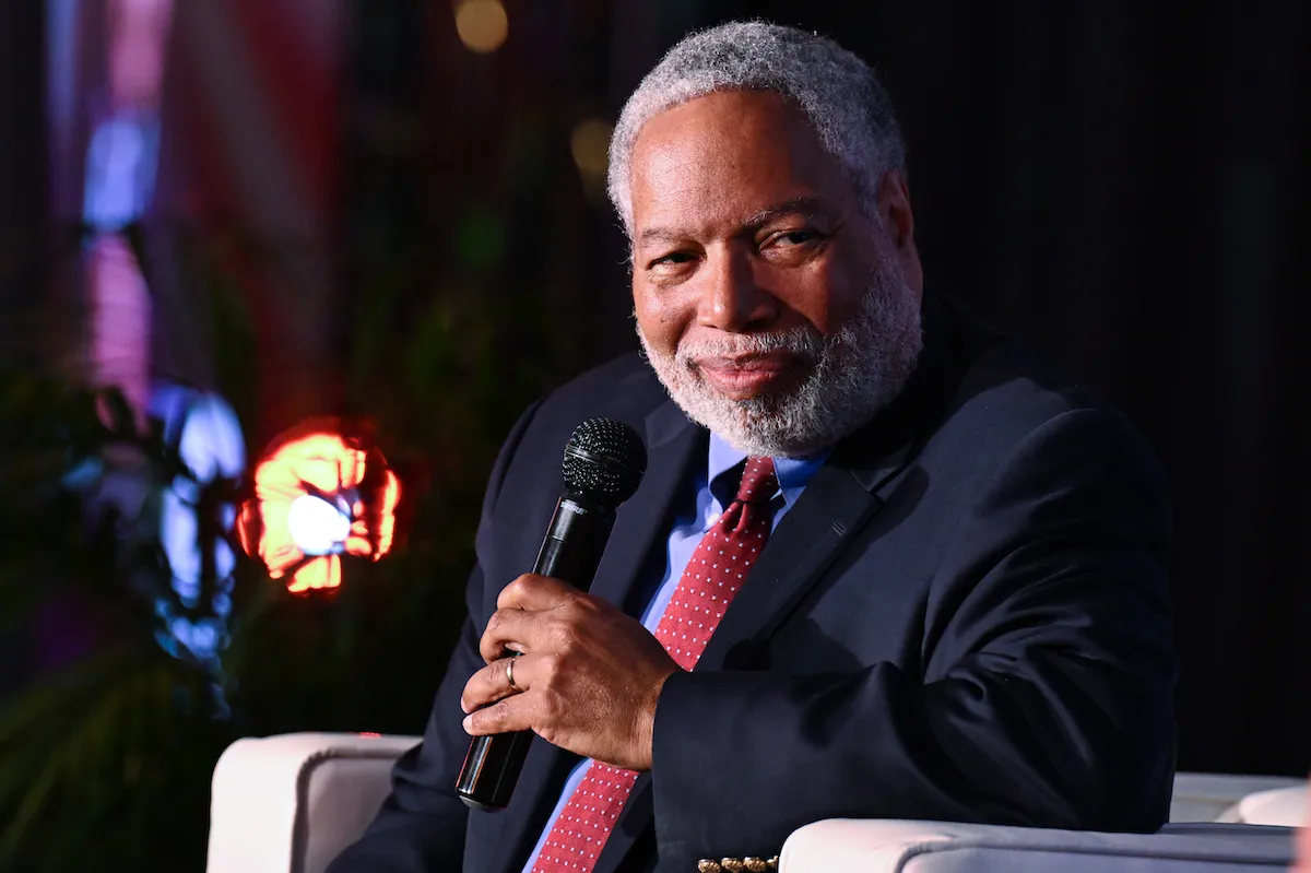 A man in a suit smiling and holding a microphone.