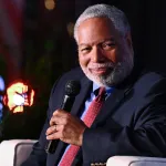 A man in a suit smiling and holding a microphone.