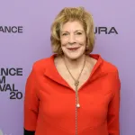A woman in an orange dress on a red carpet.