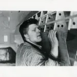 A man lifting a piece of wood and sticking out his tongue.