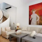 A modern living room with white sofa and gray coffee tables. On the wall is a big red drippy painting of a nurse in a face mask.