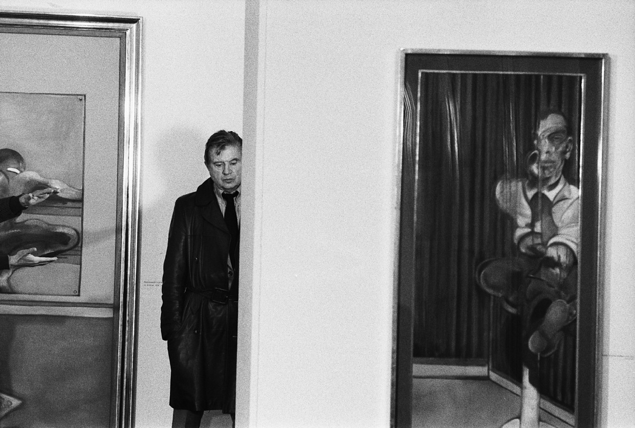 A man in a coat standing next to a painting.