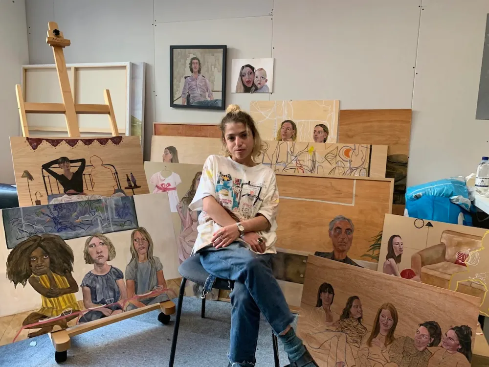 Portrait of Lorena Levi sitting cross-legged amid an array of paintings on wood.