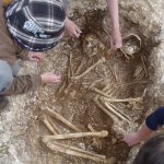 a man looks into a hole containing human remains.