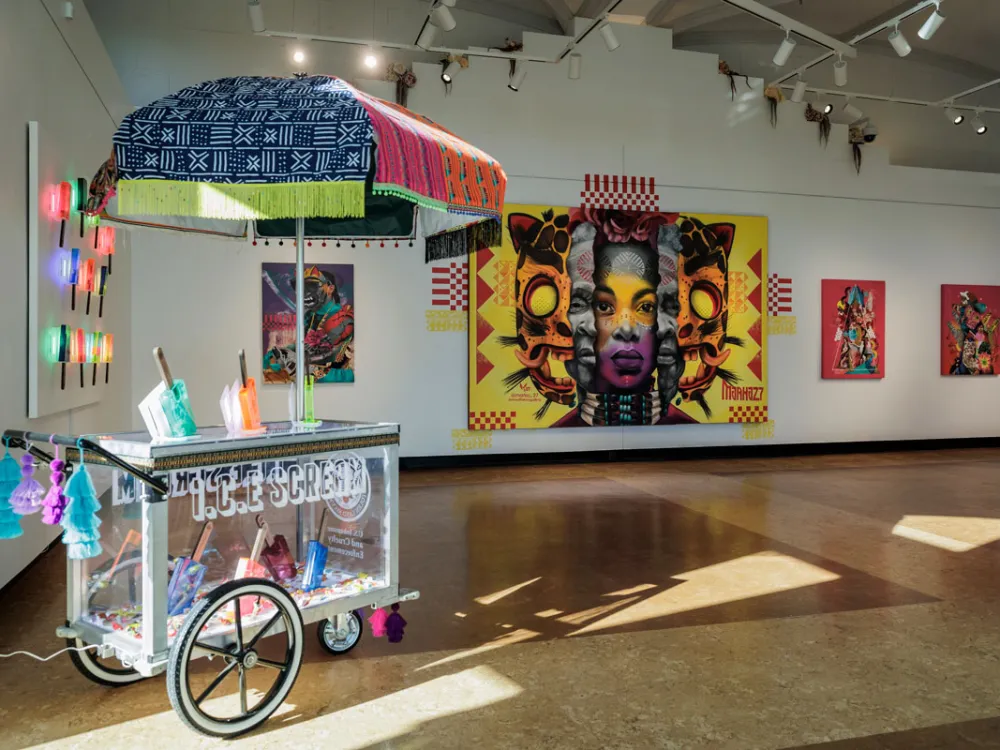 View of a university gallery exhibition with paintings on the wall and a sculpture in the foreground.