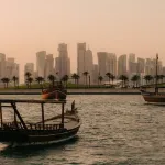 A skyline of Doha with traditional ships in the harbor.
