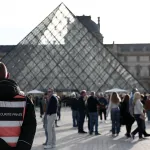 A security guard stands in front of a glass pyramid structure.