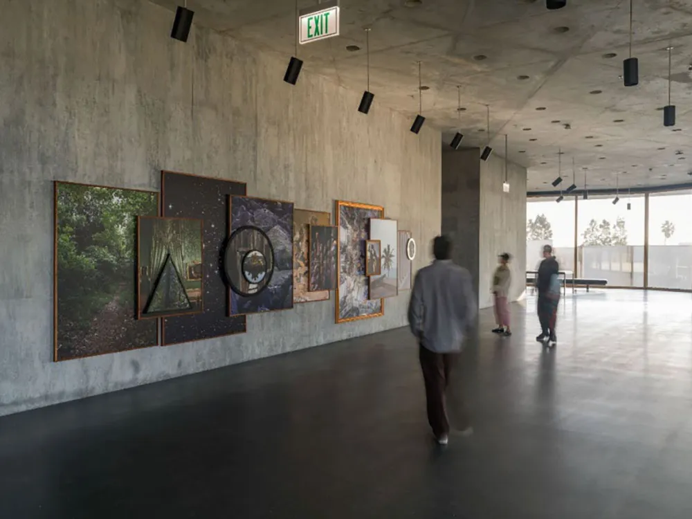 Visitors look at a photo-based, wall-hung installation on a grey concrete wall.