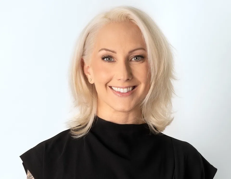 A white woman with blonde hair and a black shirt smiling.