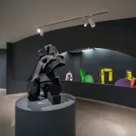 An installation composed of black crushed steel near a balcony looking out onto more steel sculptures painted bold hues.