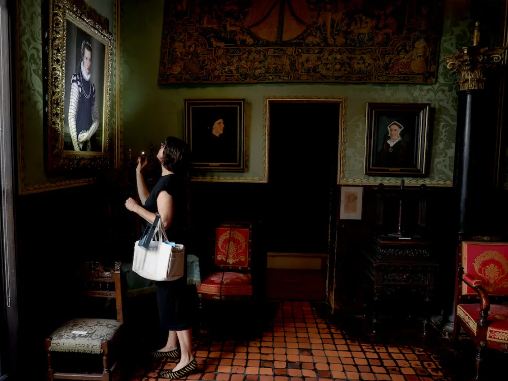 A woman peers at a painting with a flashlight in her hand.
