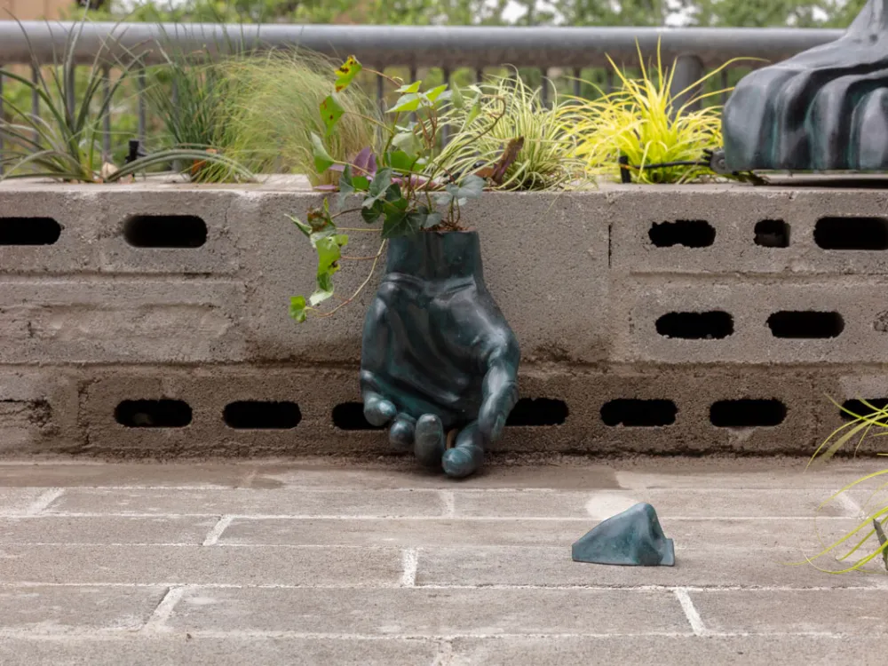 A sculpture of a hand, resting on the ground, with plants growing from the wrist.