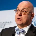 A man with a bald head, round glasses, and a bowtie.