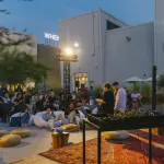 Two people read in front of an audience in the main square of Alserkal Avenue in Dubai.