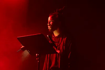 A man standing at a musical staff and speaking into a microphone.