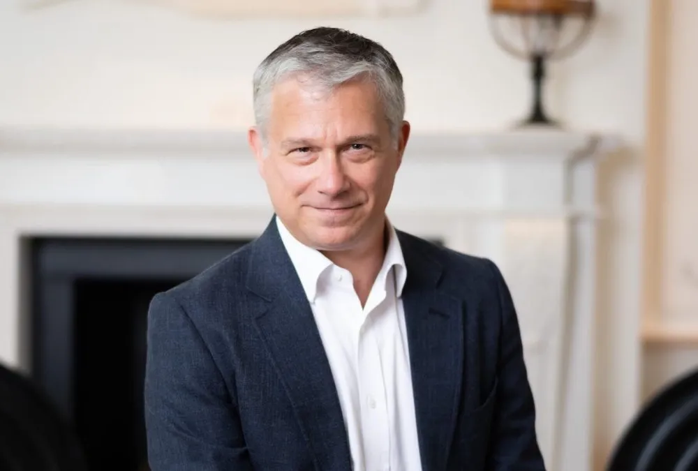 A man in a suit jacket and white shirt smiles at the camera