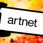 A person holding up a phone with the logo for Artnet.