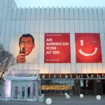 A tall white building with three banners on it, the center banner says 
