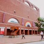 People walk in front of a tall brick building.