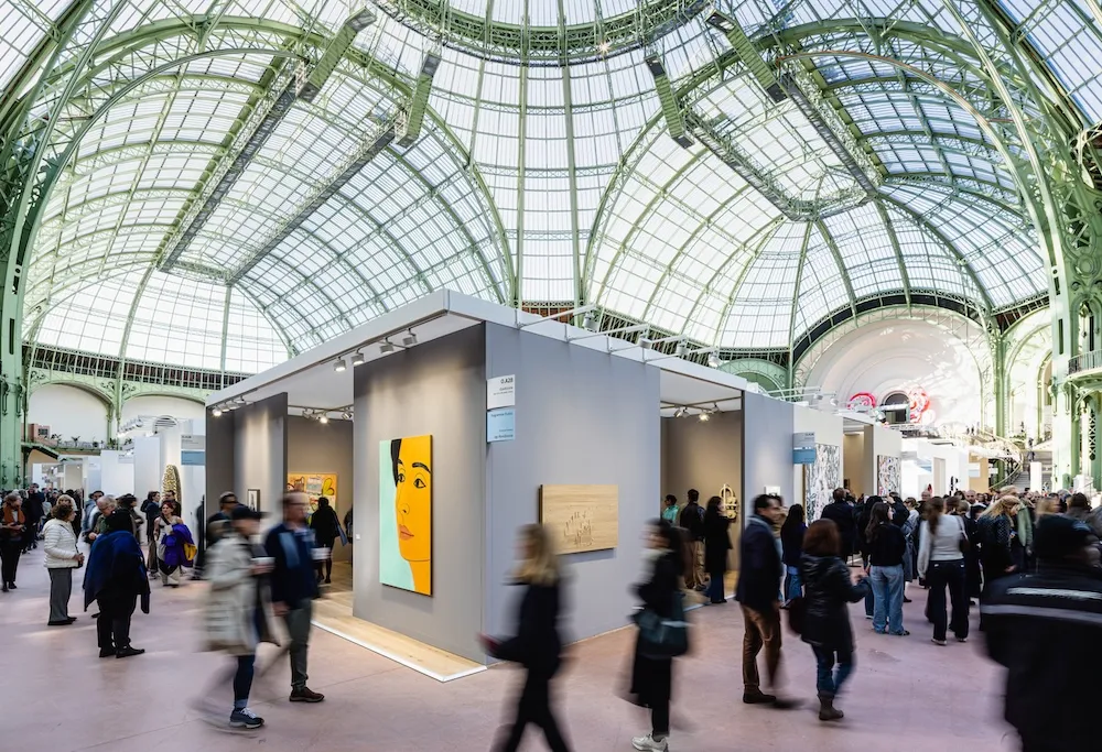 Blurred figures move through an art fair under an antique domed glass ceiling.