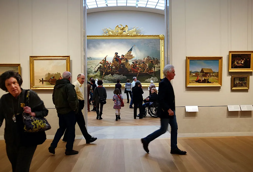 People walking around the interior galleries of a museum. In the background is a famous picture of George Washington crossing the Delaware.