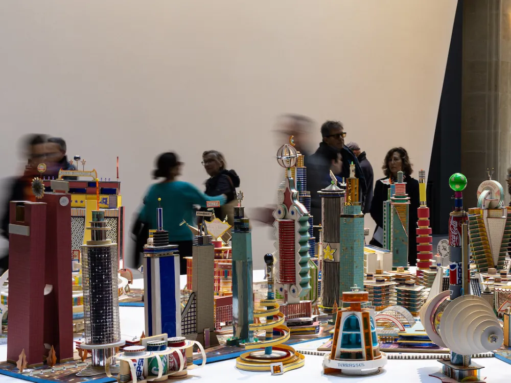 A sculpture resembling a city with many skyscrapers with people walking around it.