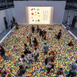 a large warehouse-like space with with a giant ball pit filled with colorful balls and people standing among them