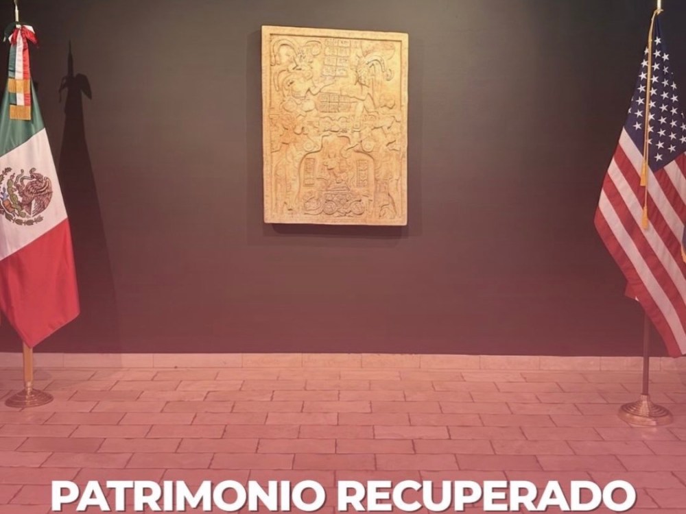 a room with a carved stone object on the wall and a Mexican flag on the left and American flag on the right