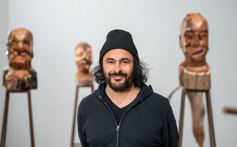 Portrait of a man in a black sweatshirt in front of several wood sculptures.