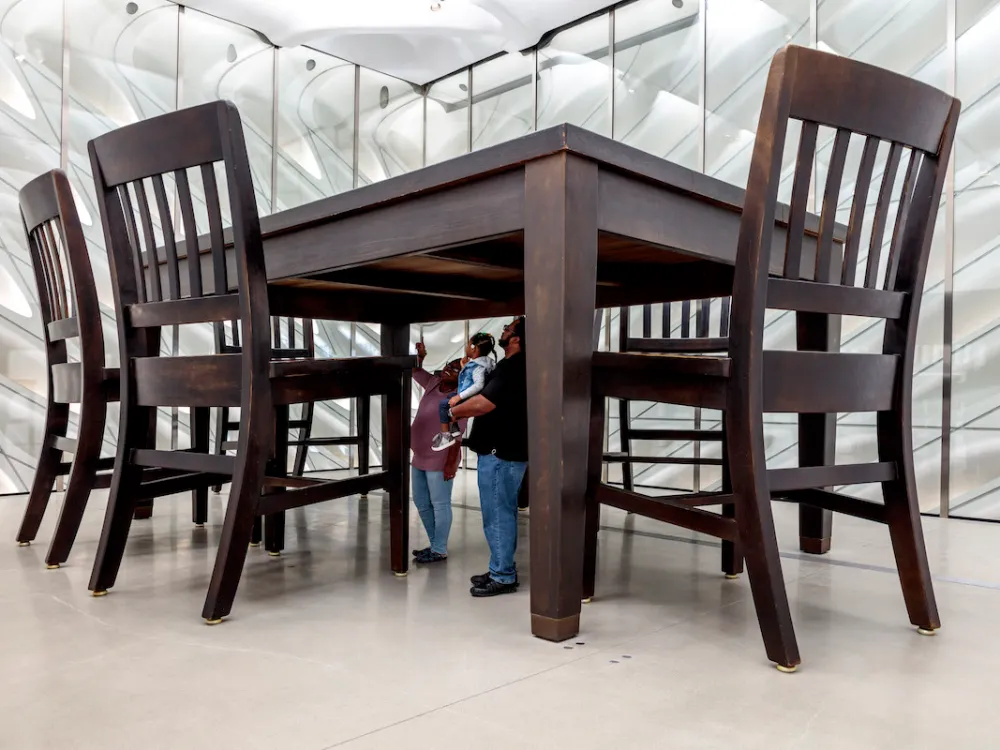 Two people looking up at an oversized wooden table and chairs.