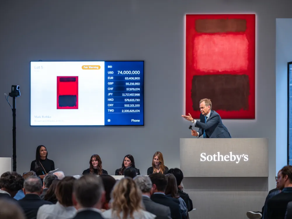 A man in a suit at a rostrum before a red abstract painting.