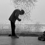 A man crouched beneath a suspended wire sculpture.