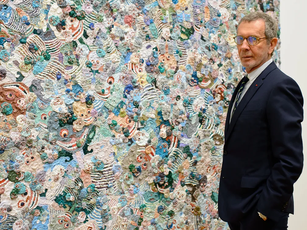 A man in a dark suit stands next to an abstract painting.