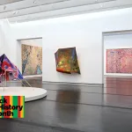 Two galleries filled with abstract paintings, some of which are unstretched and hang free from walls.
