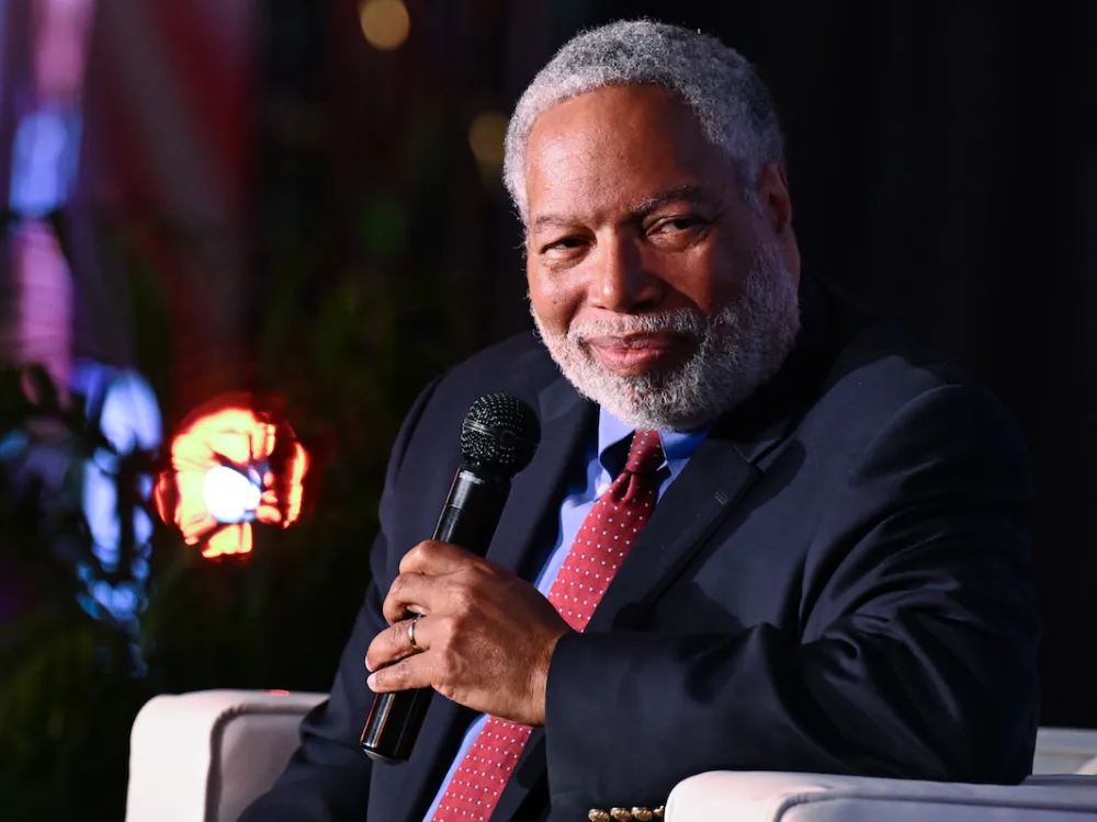 A man in a suit smiling and holding a microphone.