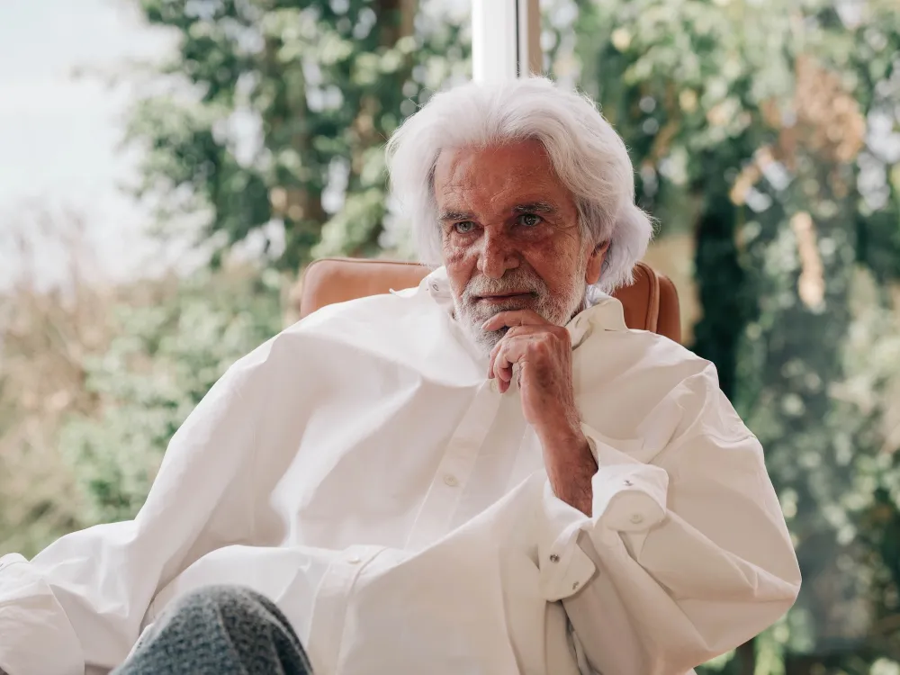 An elderly man, Brazilian art collector Bernardo Paz, is seated in a white shirt