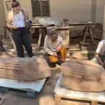 Four people surround a seven-foot-tall marble sculpture of a man, lying on its back on wooden pallets on the ground