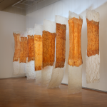 A sculptural installation composed of hanging banner-like elements, some of which are partially made of cheesecloth.